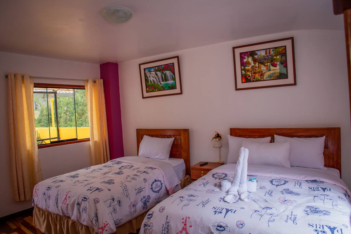A hotel room with two beds, a window with curtains, and two framed pictures on the wall.