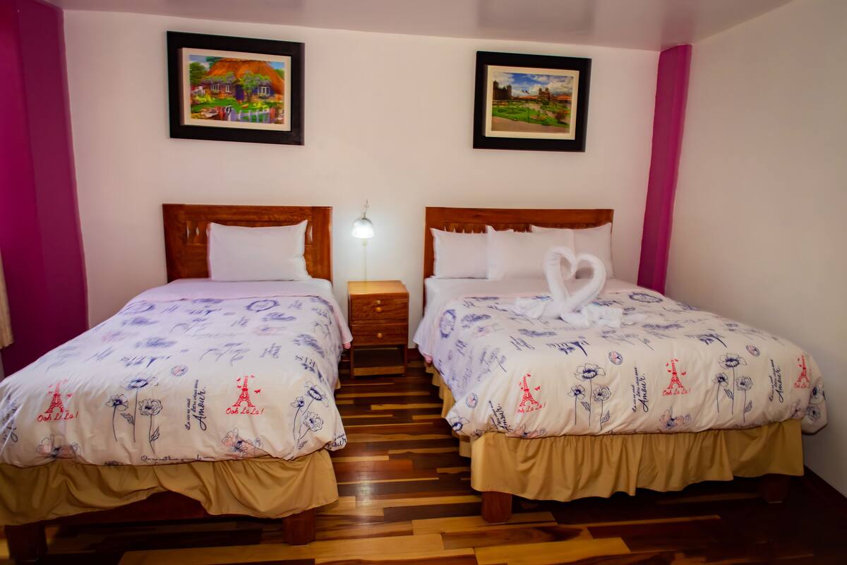 A hotel room with two beds, wooden headboards, and a nightstand between them.