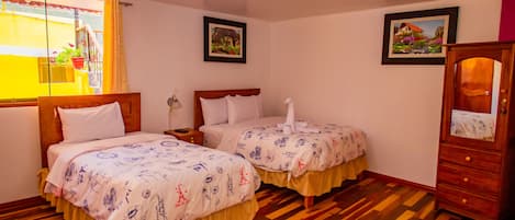 Camera d'albergo con due letti, pavimento in legno, un armadio in legno e due quadri appesi alle pareti.