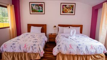 Habitación doble con dos camas, cada una con cabecero de madera, ropa de cama blanca con motivos azules y una mesita de noche con lámpara.