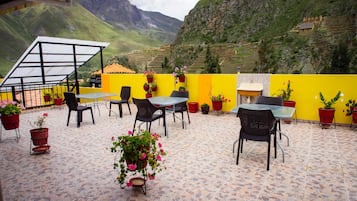 An outdoor patio with tables and chairs, surrounded by potted plants and a yellow wall.