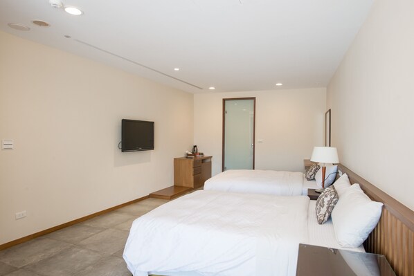 Habitación de hotel con dos camas, televisión, escritorio y mesita de noche con lámpara.