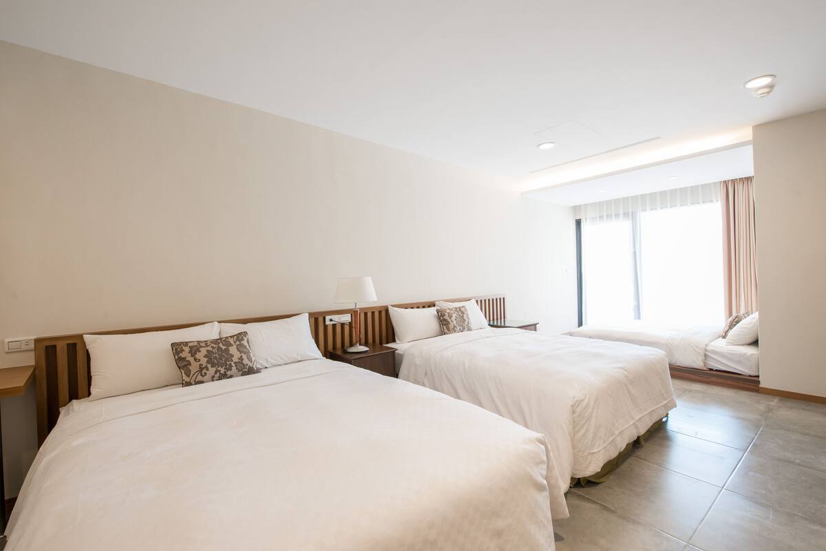 Una habitació d'hotel amb dos llits, una taula de nit, una finestra amb cortines i vista a l'exterior.