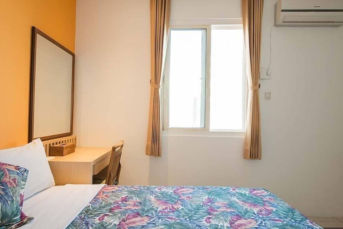 Habitació d'hotel amb llit, escriptori, cadira, finestra amb cortines i un aparell d'aire condicionat.