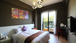 Une chambre d’hôtel moderne avec un grand lit, un bureau avec un ordinateur, un balcon avec vue et un tableau au mur.