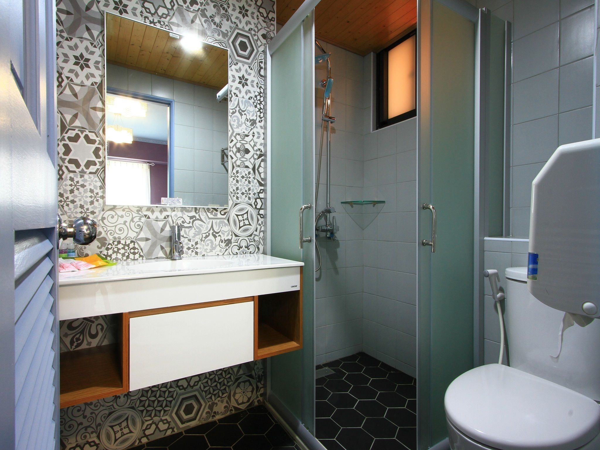 A bathroom with a patterned tile backsplash, a white sink with a mirror, a shower with a glass door, and a toilet.