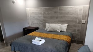 A hotel room with a large bed, a nightstand, and a chair. - Budget Inn East (Kissimmee)