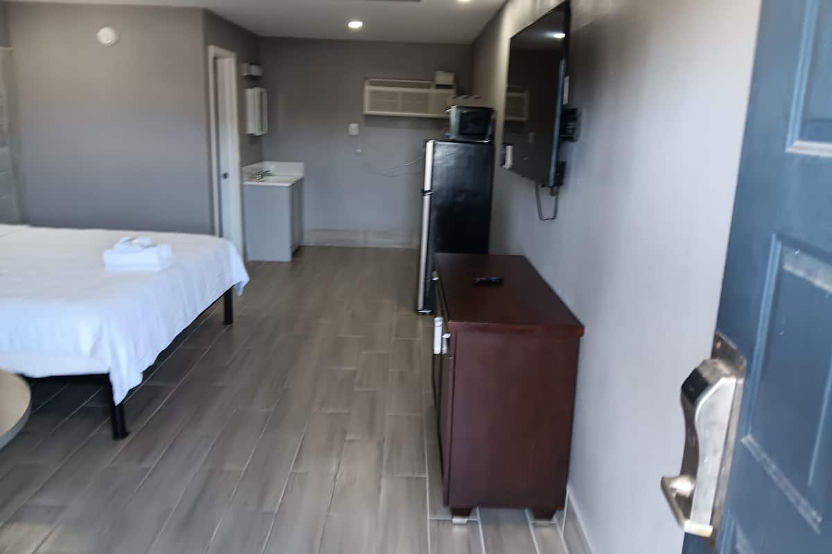 Habitación de hotel con cama, un escritorio pequeño, espejo, refrigerador y puerta.