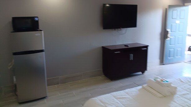 A hotel room with a bed, a flat-screen TV mounted on the wall, a minibar, and a door leading to another room. - Budget Inn East (Kissimmee)