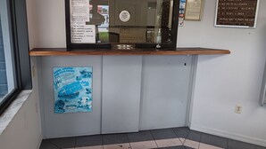 A reception desk with a glass partition, a bulletin board with posted notices, and a welcome sign for Budget Inn East. - Budget Inn East (Kissimmee)
