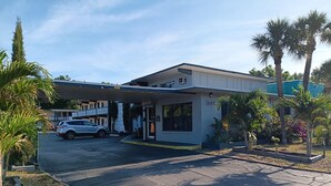 A hotel with a covered parking area, palm trees, and a building number 307. - Budget Inn East (Kissimmee)