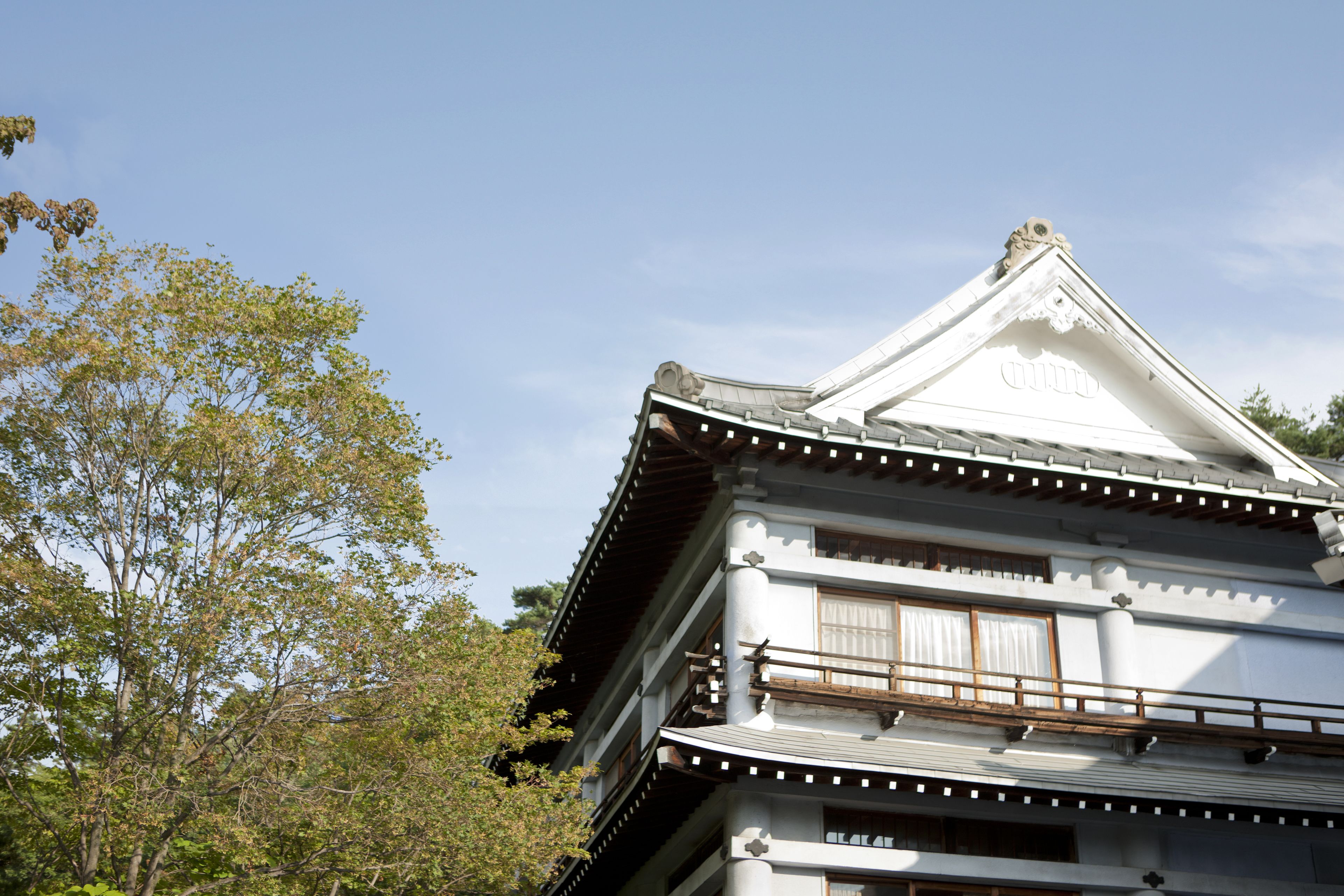 A traditional Japanese building with a white facade, wooden balcony railings, and a tiled roof.