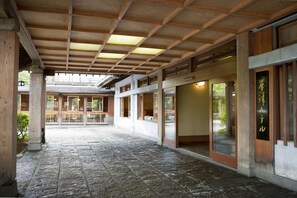 A covered walkway with stone flooring, wooden beams, and glass doors leading to a building with traditional Japanese architecture. - Kusatsu Hotel (Kusatsu)
