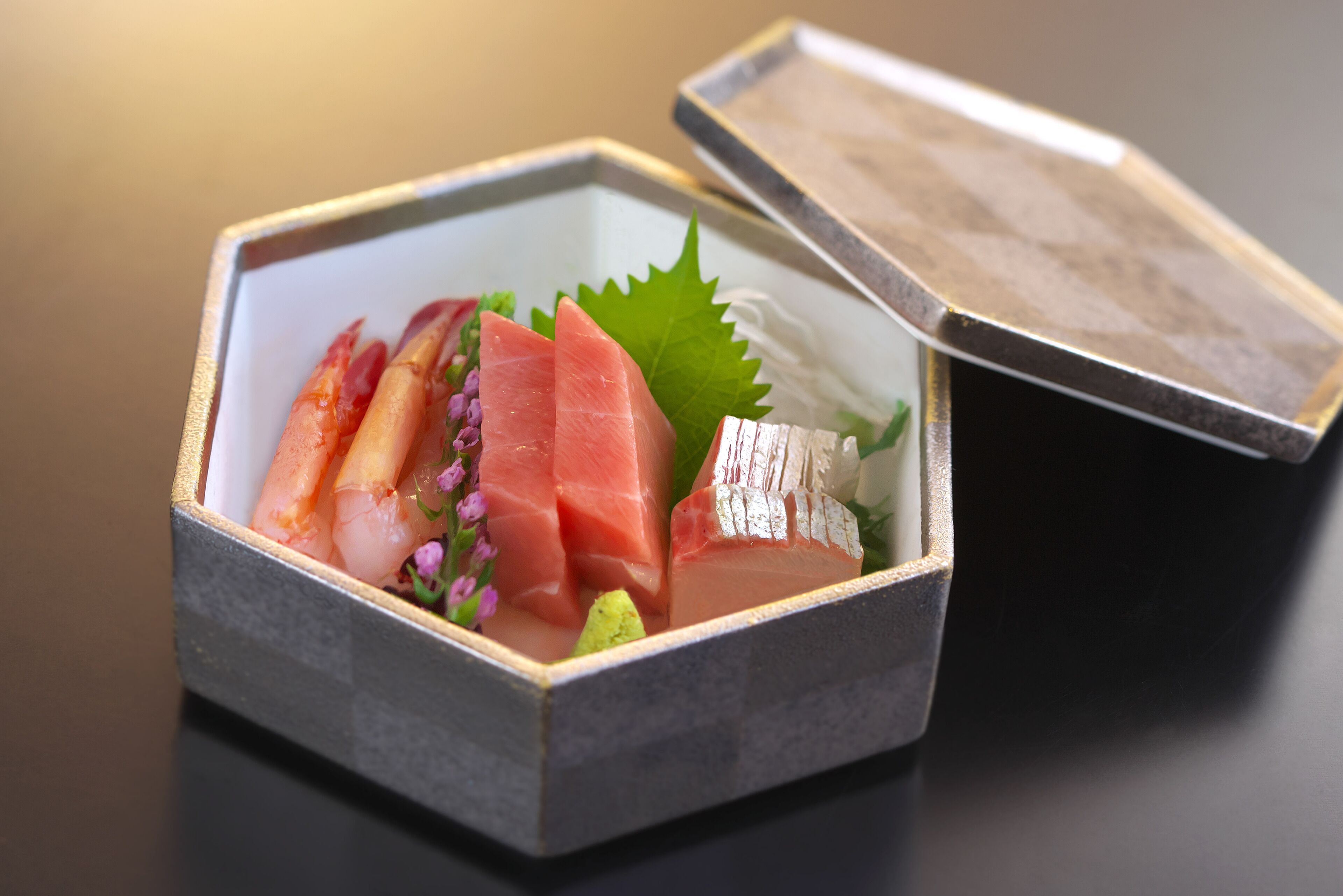 Una caja hexagonal que contiene varios tipos de sashimi, incluyendo salmón y atún, con tapa de madera.