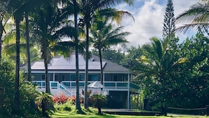 A two-story house with a white exterior, surrounded by lush greenery and palm trees. - Ala Kai Bed & Breakfast (Keaau)