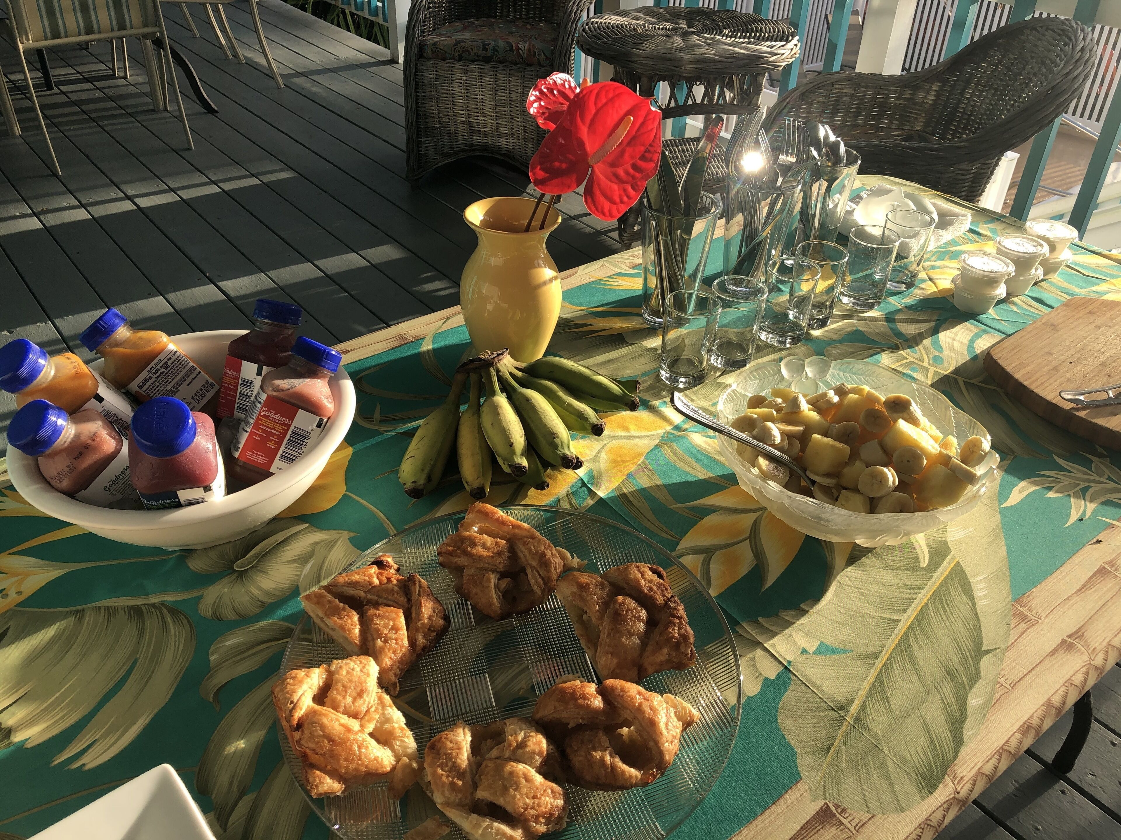 Une table dressée avec différents aliments, notamment un saladier de fruits, une assiette de pâtisseries et un vase avec une fleur rouge.