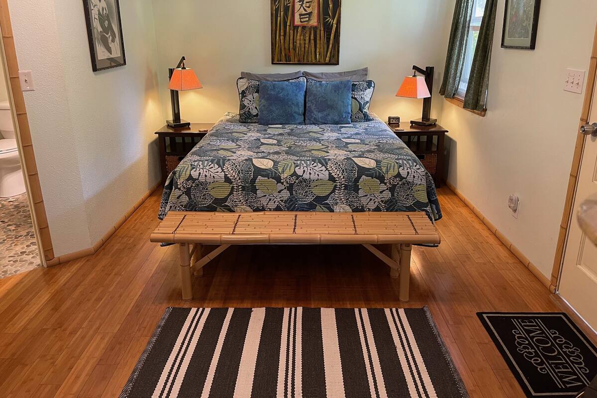 A bedroom with a bed, two nightstands, a wooden bench, a black and white striped rug, and artwork on the walls.