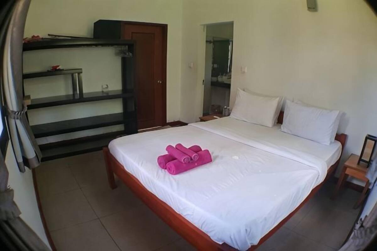 A hotel room with a bed, a wooden nightstand, a mirror, and a wardrobe.