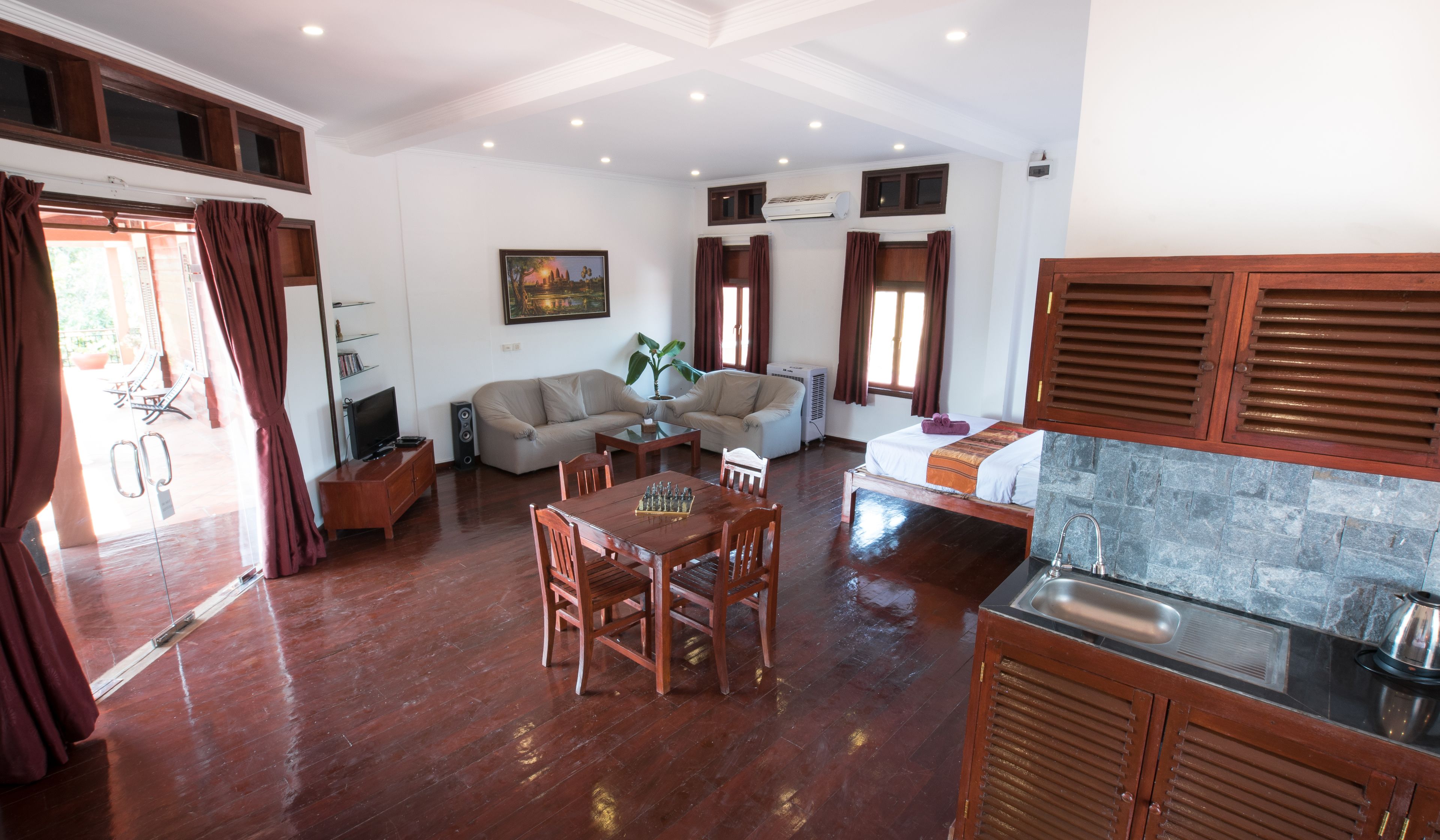 A spacious living area with a wooden dining table, sofas, and a kitchen area with a sink and stove.