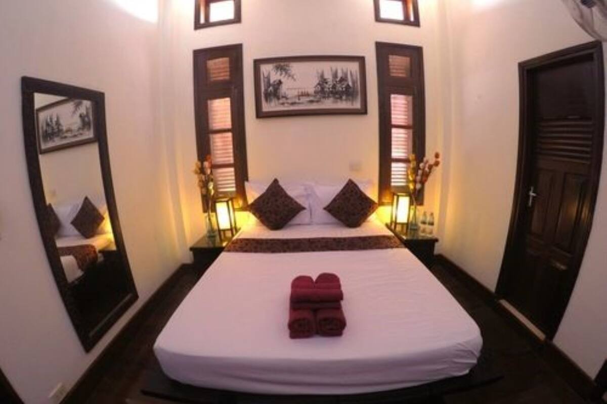 A hotel room with a bed, pillows, a nightstand, a mirror, and a door.