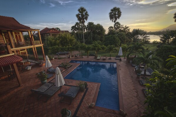 Un área de piscina con sillones de descanso, sombrillas y vistas a un cuerpo de agua.
