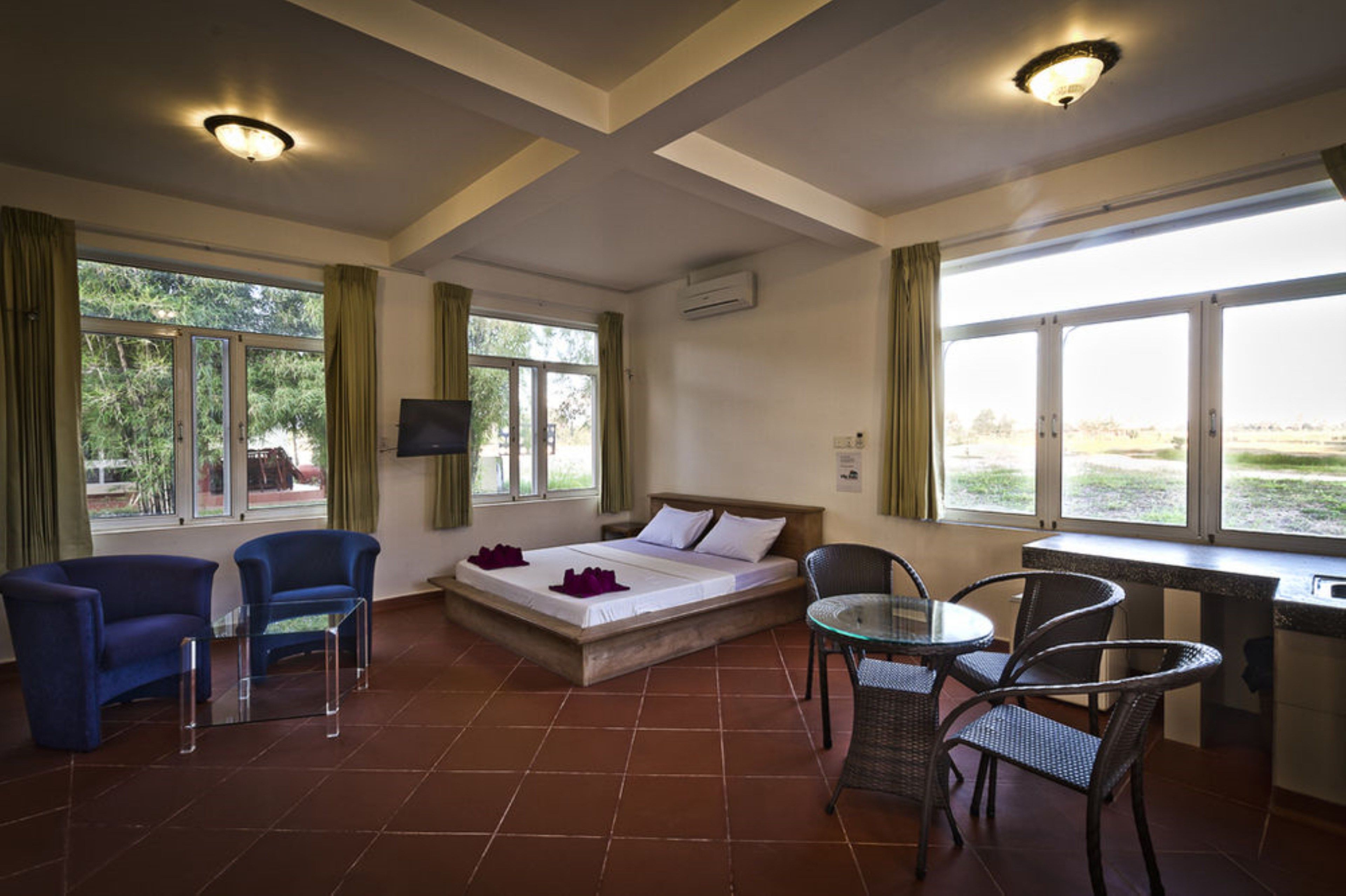 A hotel room with a bed, two chairs, a small table, and large windows with curtains.