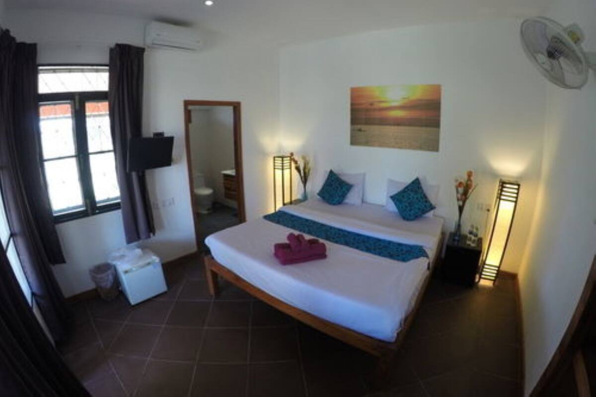 A bedroom with a bed, a bedside table, a mirror, a window with curtains, a wall-mounted fan, and a painting.