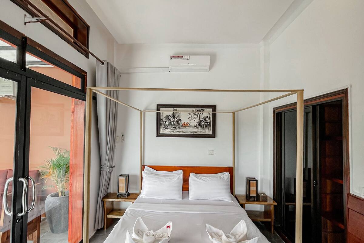 A modern bedroom with a four-poster bed, a large window, and a sliding glass door leading to a balcony.
