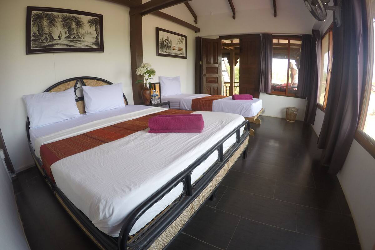 A hotel room with a large bed, two smaller beds, wooden beams, and artwork on the walls.
