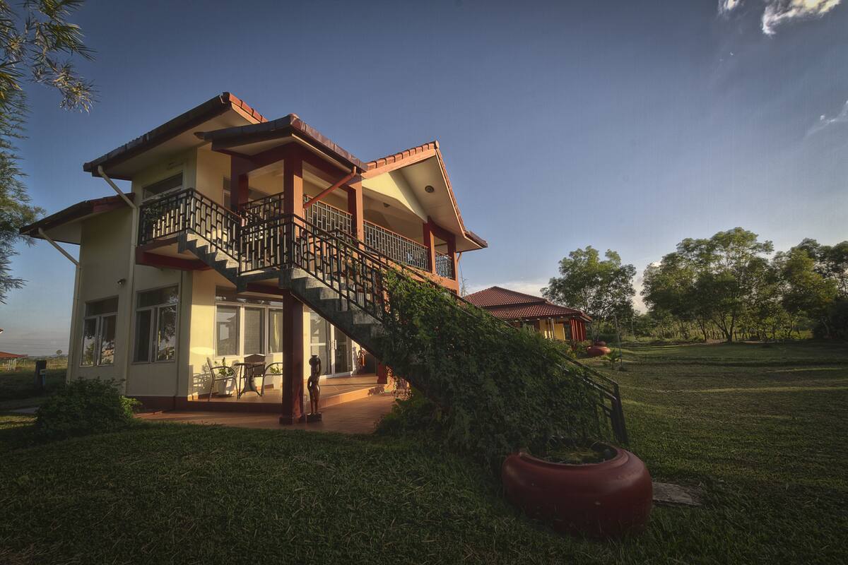 A two-story house with a balcony, a staircase, and a large lawn.