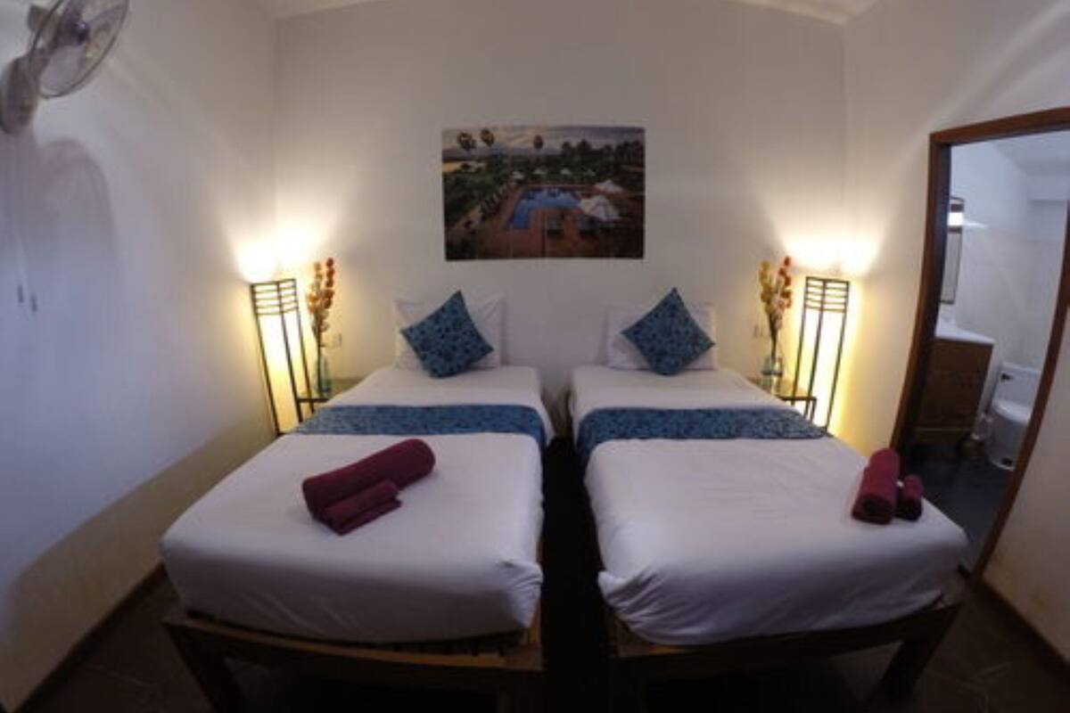 A room with two beds, each with a blue and white bedspread, a red towel on one bed, and a painting on the wall.