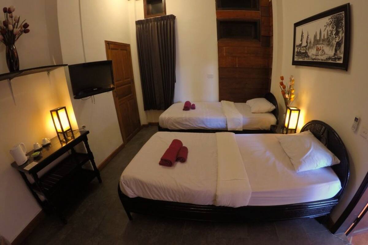 A hotel room with two beds, a TV, a desk with a lamp, and a painting on the wall.