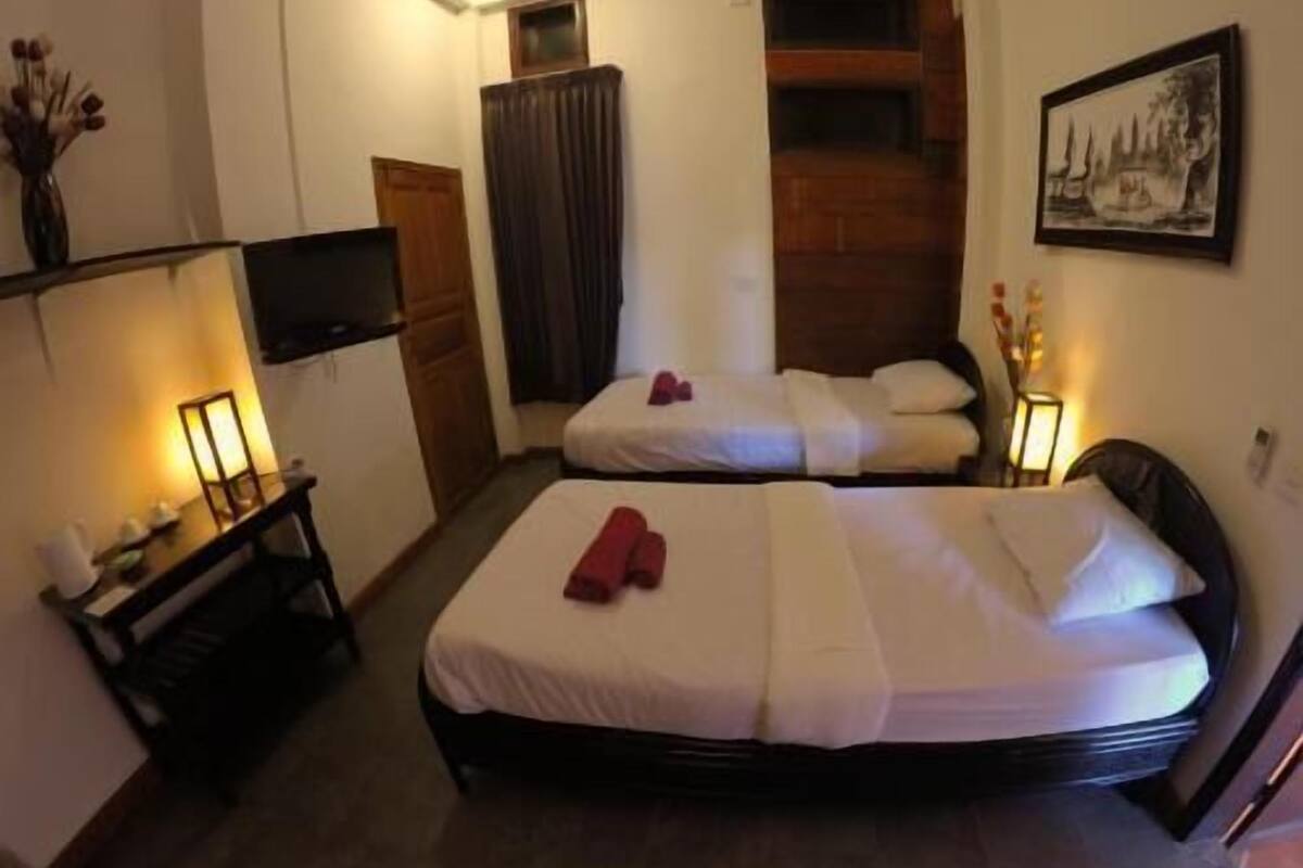 A hotel room with two beds, a desk with a lamp, a TV, and a painting on the wall.