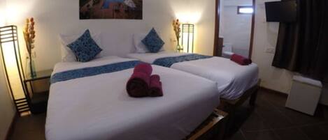 A hotel room with two beds, a painting on the wall, a mirror, a TV, and a small table with a vase.