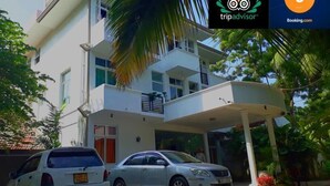 A two-story building with a balcony on the second floor, a covered entrance, and two cars parked in front. - Nooit Gedacht Holiday Resort (Unawatuna)