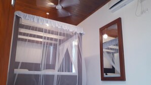 A bedroom with a bed covered by a sheer canopy, a ceiling fan, and an air conditioning unit. - Nooit Gedacht Holiday Resort (Unawatuna)
