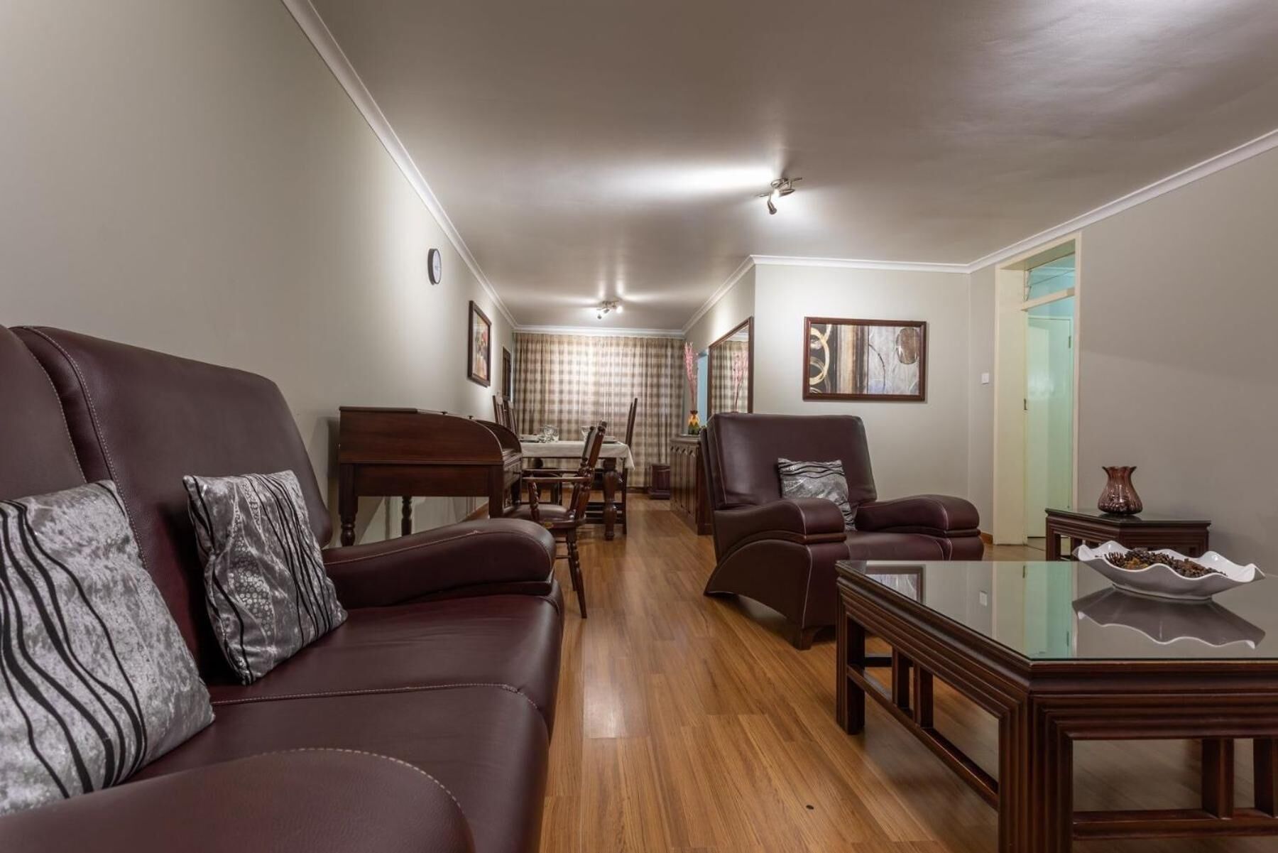 Un salon spacieux avec un canapé en cuir marron foncé, une table basse en bois et un coin repas à l’arrière-plan.