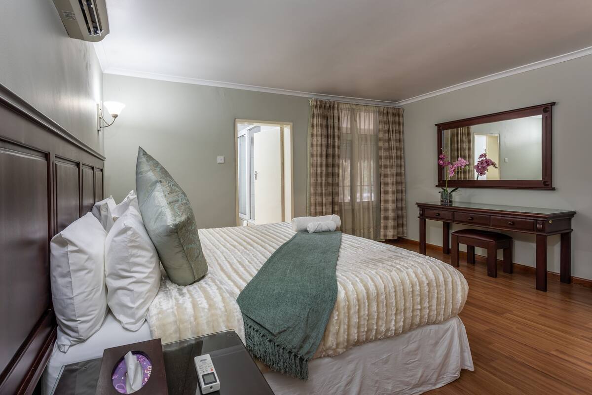 A hotel room with a bed, a desk, a mirror, and a window with curtains.