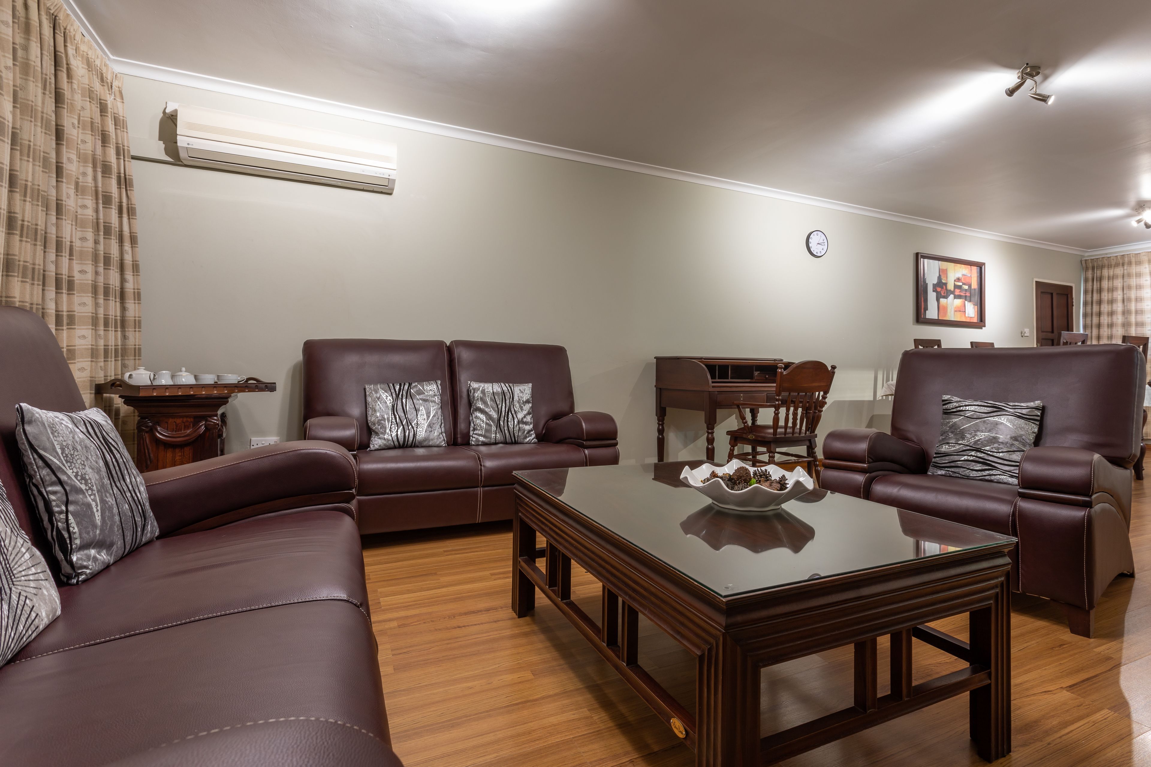 A living room with a brown leather sofa, a glass coffee table, and a wooden side table with a teapot.