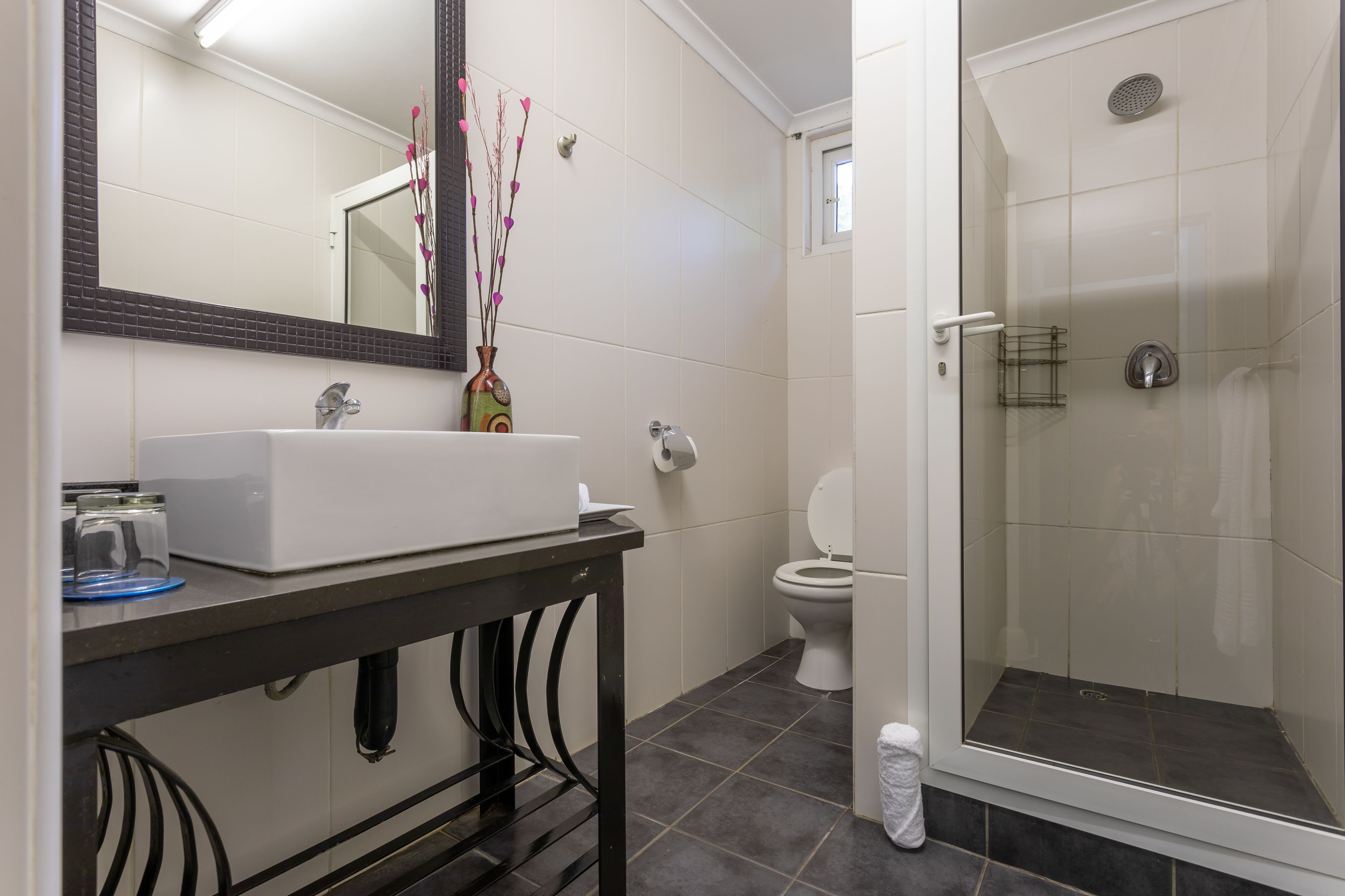 Un baño con lavamanos blanco, un espejo, inodoro y ducha con mampara de vidrio.