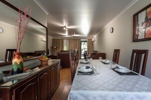A dining area with a long table set for four, a vase with branches, and a view into the living room.