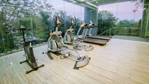 A gym with cardio machines and a treadmill, large windows with a view of greenery.