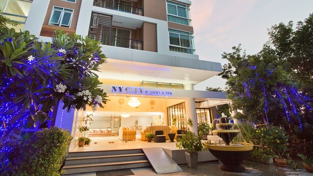 A modern hotel with a visible entrance, outdoor seating area, and a water feature.
