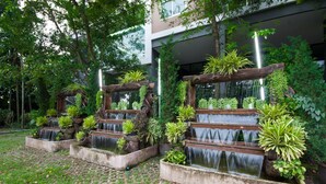 A courtyard with multiple water features, surrounded by lush greenery and a modern building in the background.