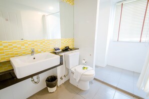 Bathroom features a white sink, toilet, and mirror above a yellow and white tiled wall with a window.