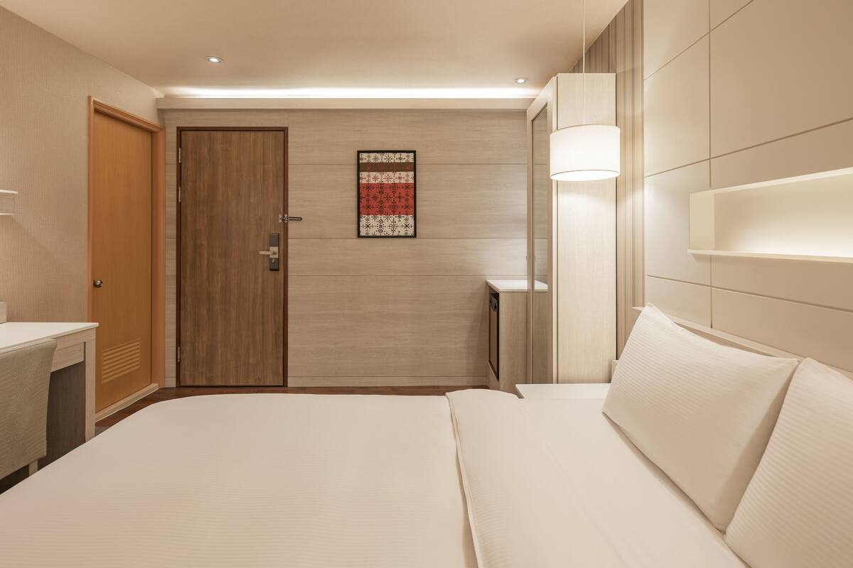 A hotel room with a bed, bedside table, lamp, and a door with a wooden panel.