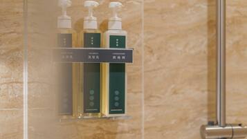 A bathroom with a glass shelf holding three bottles of toiletries labeled 'BODY WASH,' 'SHAMPOO,' and 'CONDITIONER.'