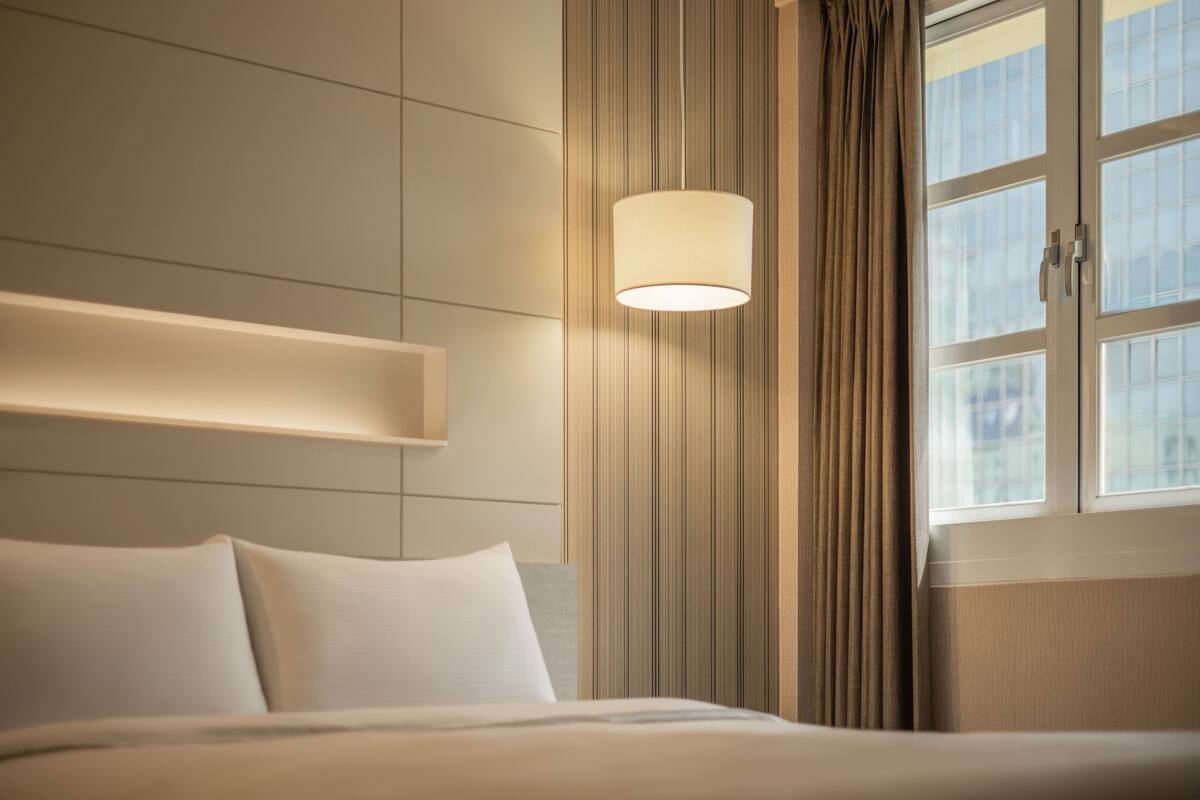 A hotel room with a bed, a bedside lamp, a window with curtains, and a view of the outside.
