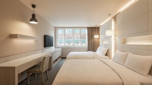 A hotel room with a desk, two beds, a television, and a large window with curtains.