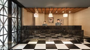A reception area with a checkered floor, marble reception desk, wooden ceiling beams, and pendant lighting.